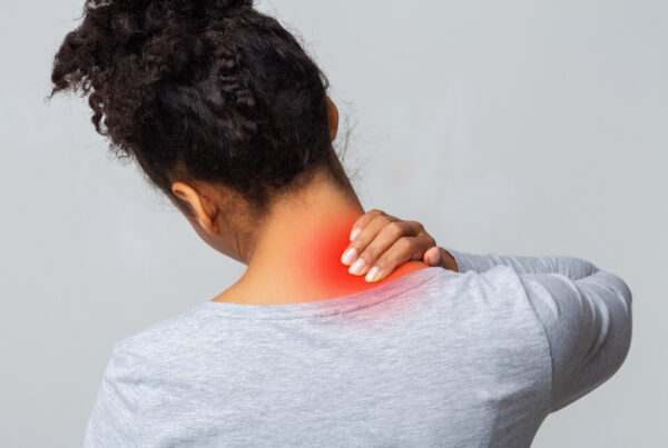 Woman holding the back of her sore neck, with the painful area highlighted in red